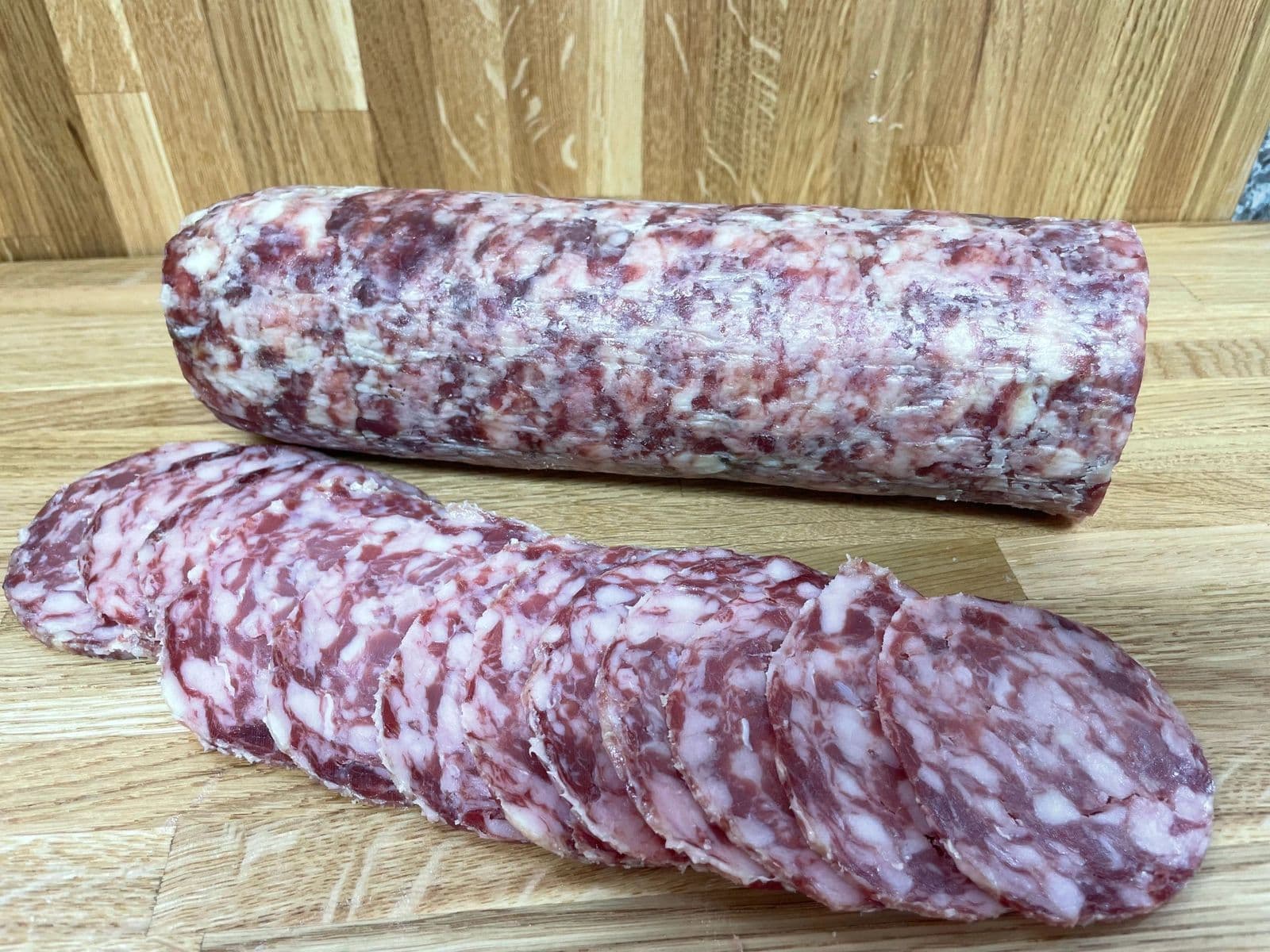 A whole salami with slices on a wooden board